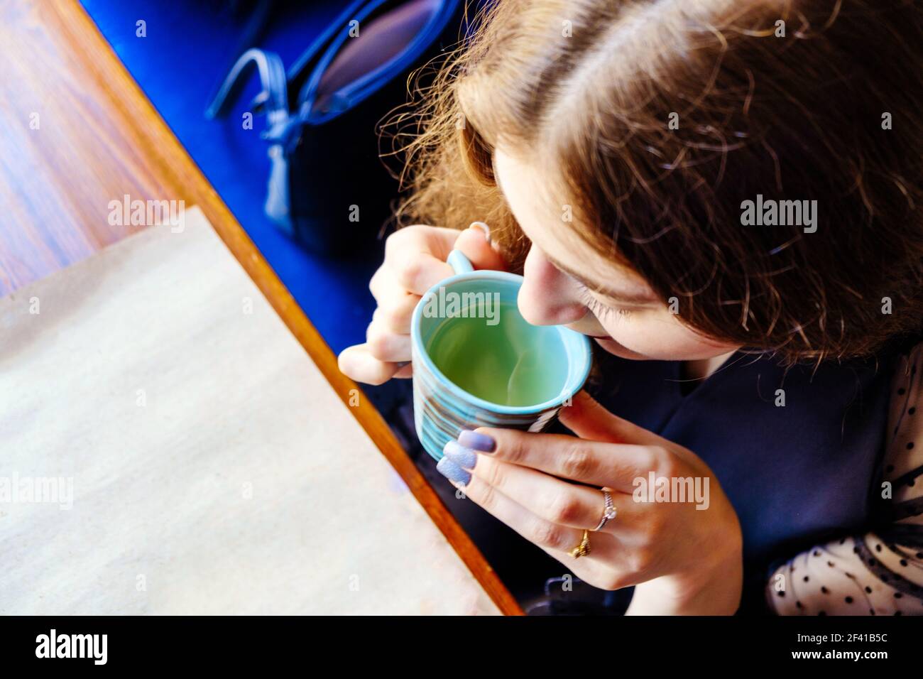 Vue d'en haut d'une jeune femme qui boit du café d'une petite tasse en céramique. À côté du canapé se trouve un sac à main pour dame. CopySpace se trouve sur le papier artisanal au-dessus du plan d'examen. Vue d'en haut d'une jeune femme qui boit du café d'une petite tasse en céramique. À côté du canapé se trouve un sac à main pour dame. Banque D'Images