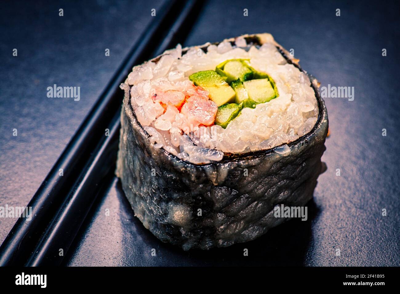 Prise de vue en rouleau de sushi sur fond noir avec reflets, tons d'image dans une couleur vintage. Macro de sushi servi sur fond noir avec réflexion avec baguettes. Macro sushi servi sur noir avec reflet Banque D'Images