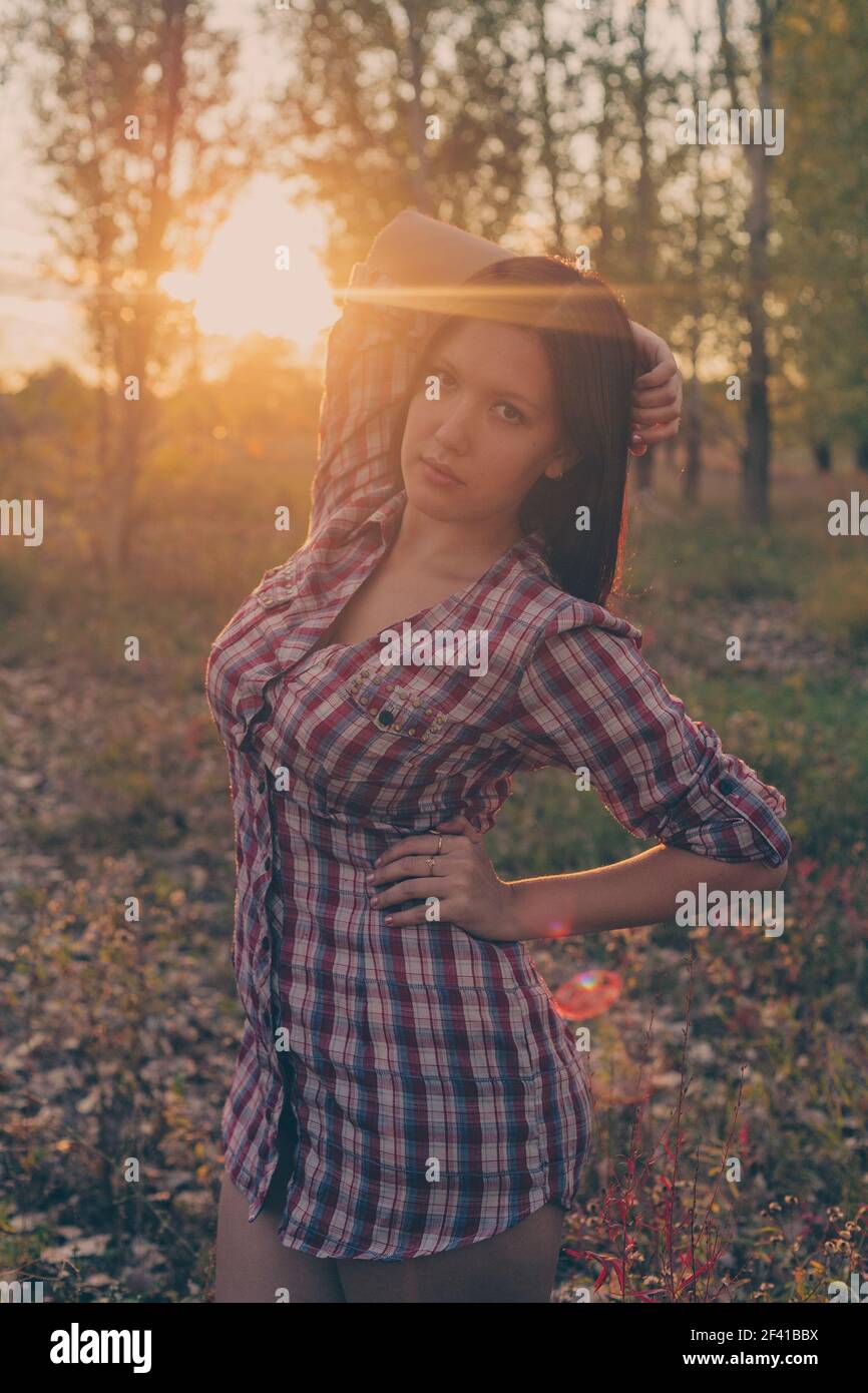 Une jeune fille calme se posant dans un parc boisé à l'heure automnale au coucher du soleil vêtue d'une chemise à carreaux. Banque D'Images