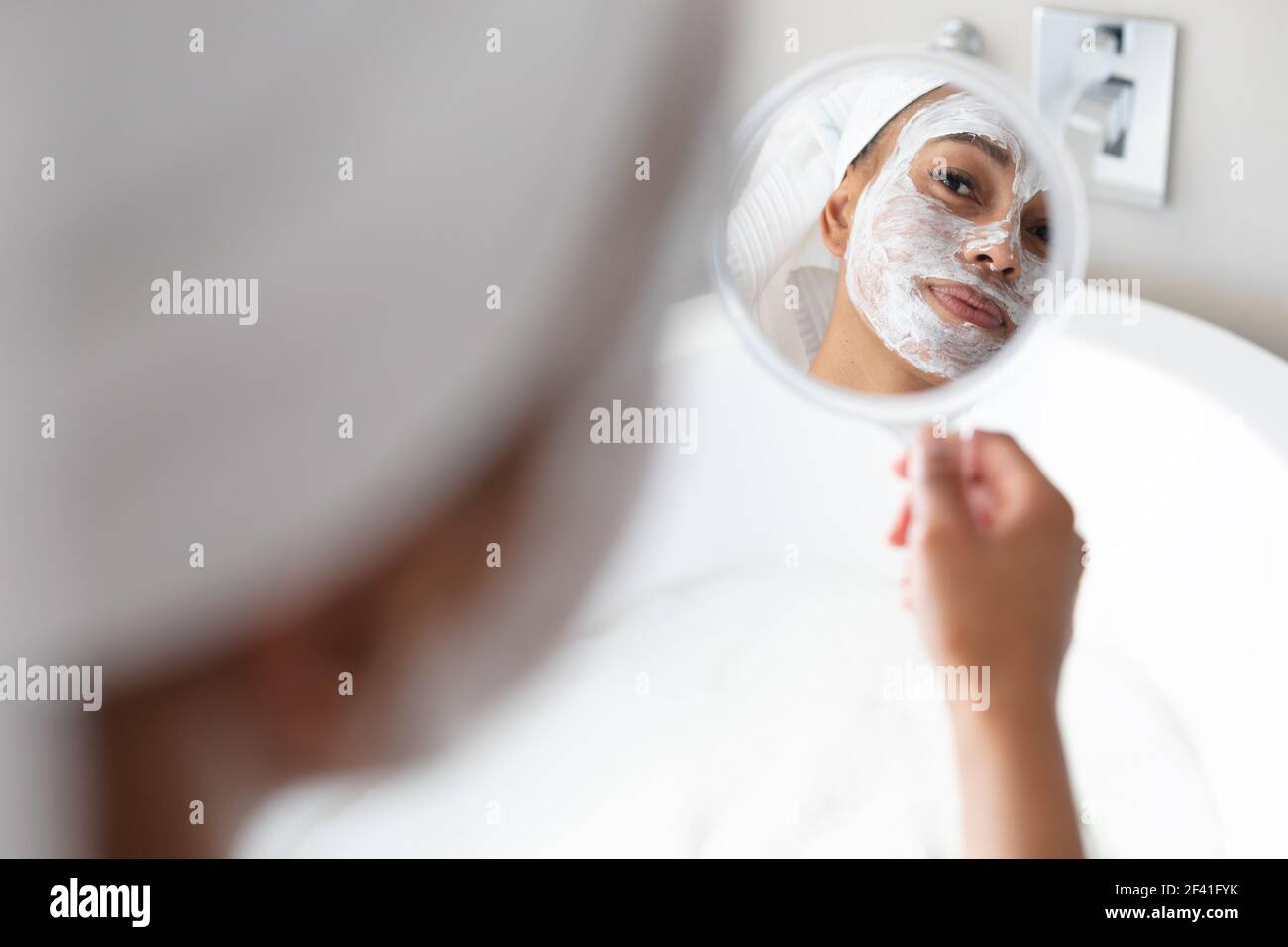 Femme afro-américaine avec masque facial tenant un miroir salle de bains Banque D'Images