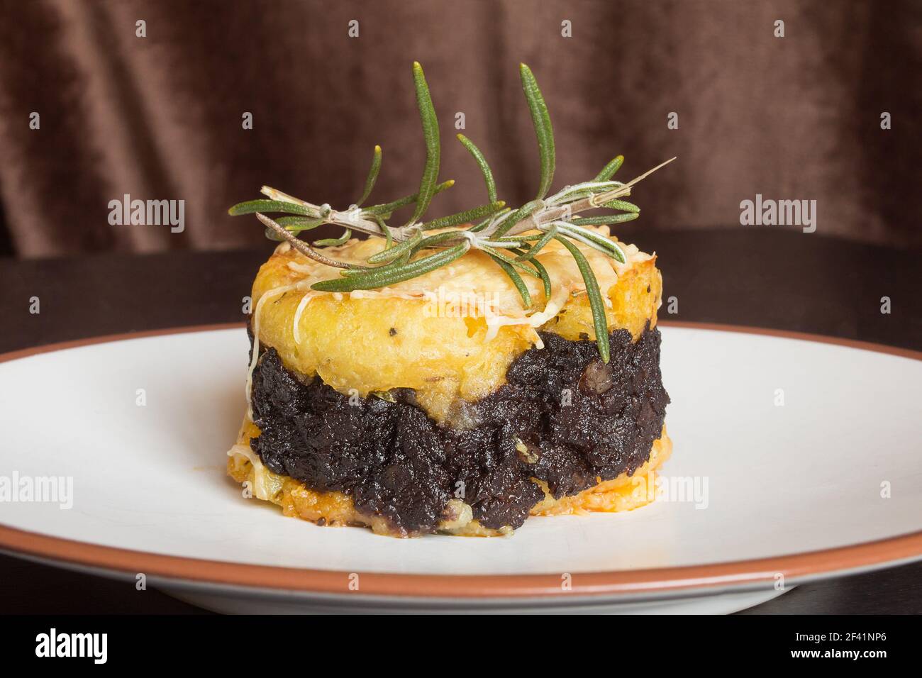 Gros plan d'un gâteau de pommes de terre au beurre avec crème de pudding  noire au chocolat, fromage râpé et une branche fraîche de romarin sur une  table en bois Photo Stock -