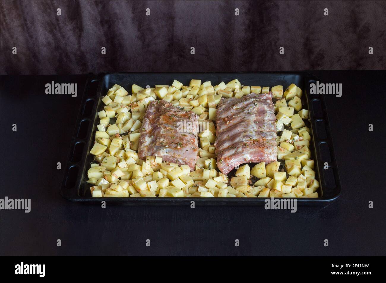 Lanières de côtes de porc fraîches entourées de pommes de terre avec sauce au vinaigre d'huile d'ail et origan sur une plaque de cuisson aliments et viandes. Banque D'Images