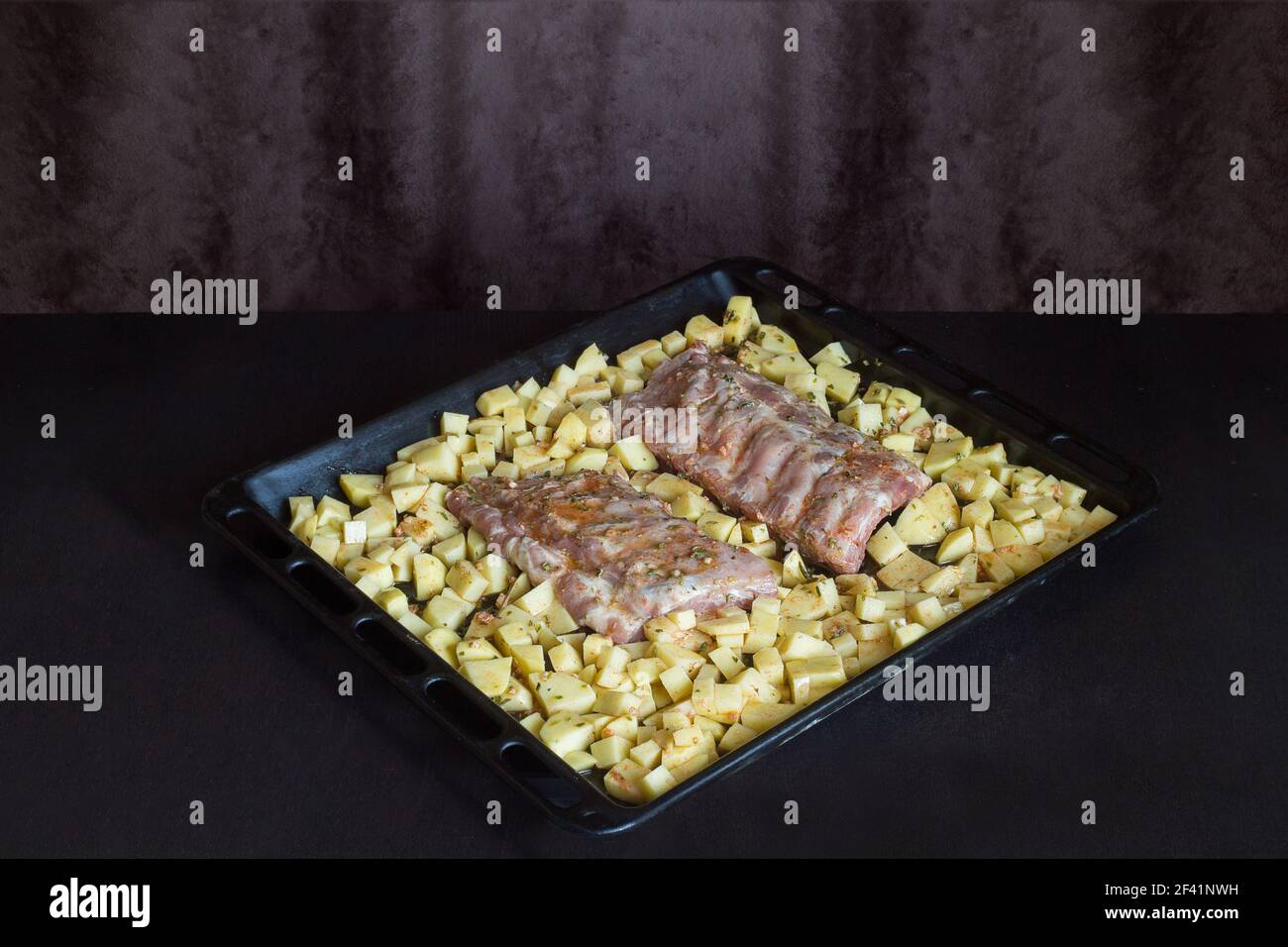 Deux bandes de côtes de porc fraîches entourées de pommes de terre sur une plaque de cuisson. Plats frais et viandes crues sur une table en bois. Banque D'Images