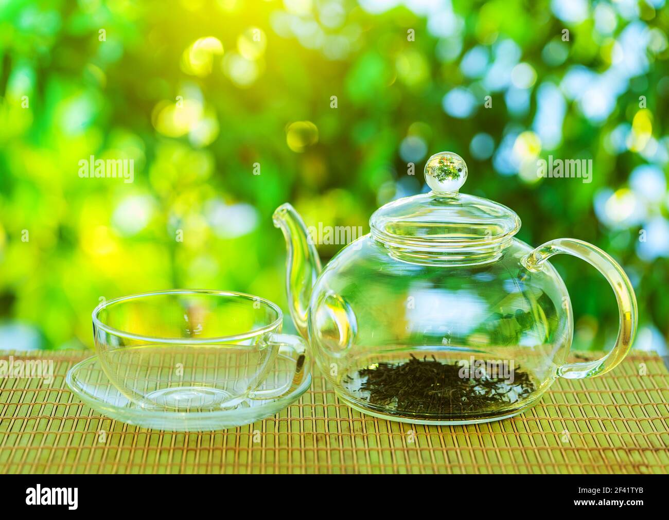 Cérémonie du thé. Une théière en verre vide avec des feuilles de thé se dresse sur une table en bois sur le fond d'une belle nature avec bokeh. Banque D'Images