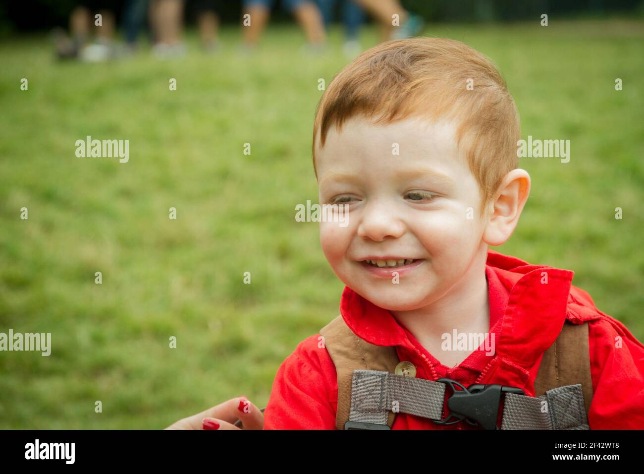 Portrait d'un joli bébé à tête rouge aux yeux bleus souriant portant une veste rouge dans un parc. Banque D'Images