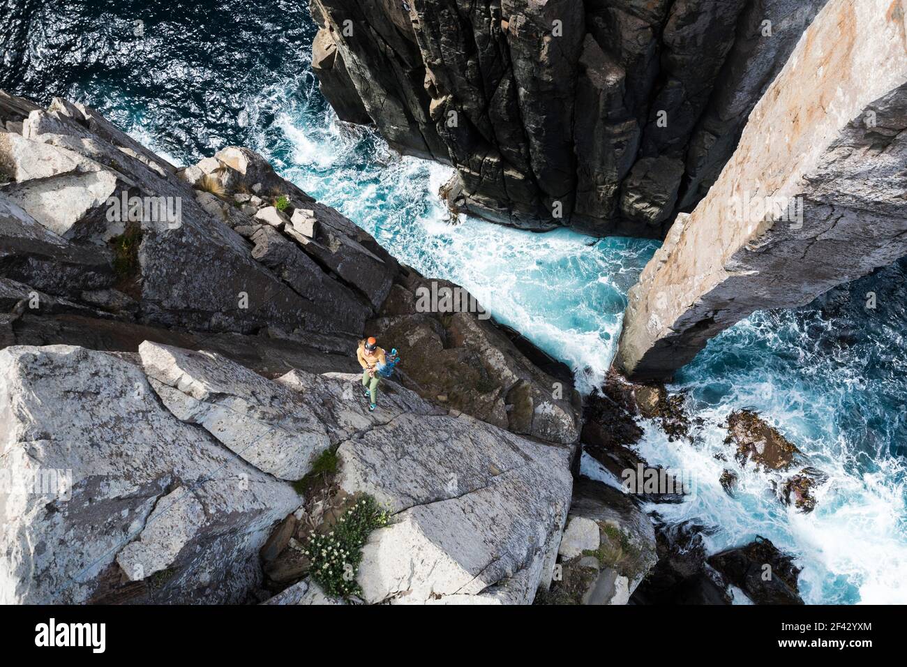 Une femme aventureuse sourit alors qu'elle descend du bord d'une falaise jusqu'au fond du Totem Pole, une colonne de roche qui émerge de l'océan à Cape Hauy, Tasmanie Banque D'Images