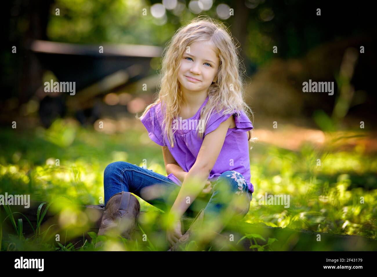 Belle petite fille blonde en chemise violette assise sur l'herbe. Banque D'Images