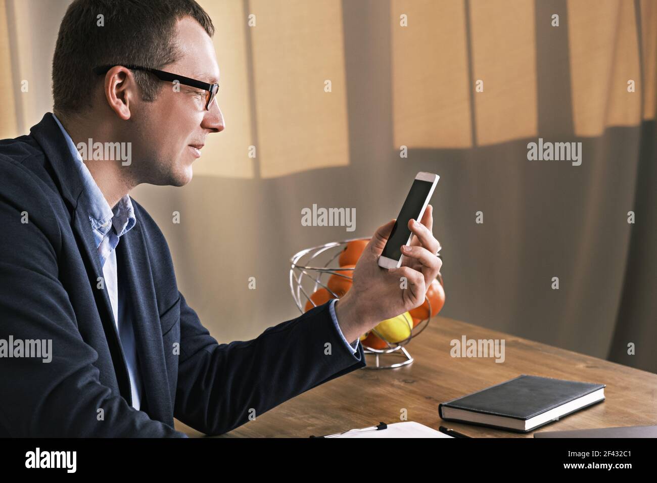 Jeune homme d'affaires portant un costume et des lunettes regardant son mobile téléphone assis à une table Banque D'Images