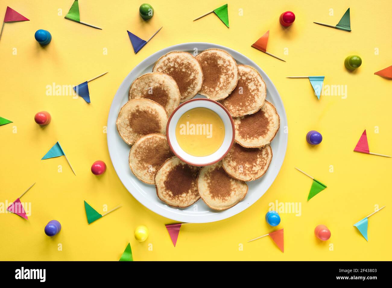 Assiette de petites crêpes rondes avec drapeaux de fête colorés sur fond en papier à trois couches de couleur. Vue de dessus, couleurs vives et vives, orange Banque D'Images