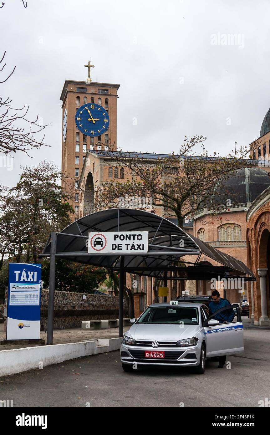 Un espace réservé pour le service de taxi avec une voiture en argent garée sous un auvent à proximité de la basilique notre-Dame d'Aparecida, sous ciel couvert. Banque D'Images