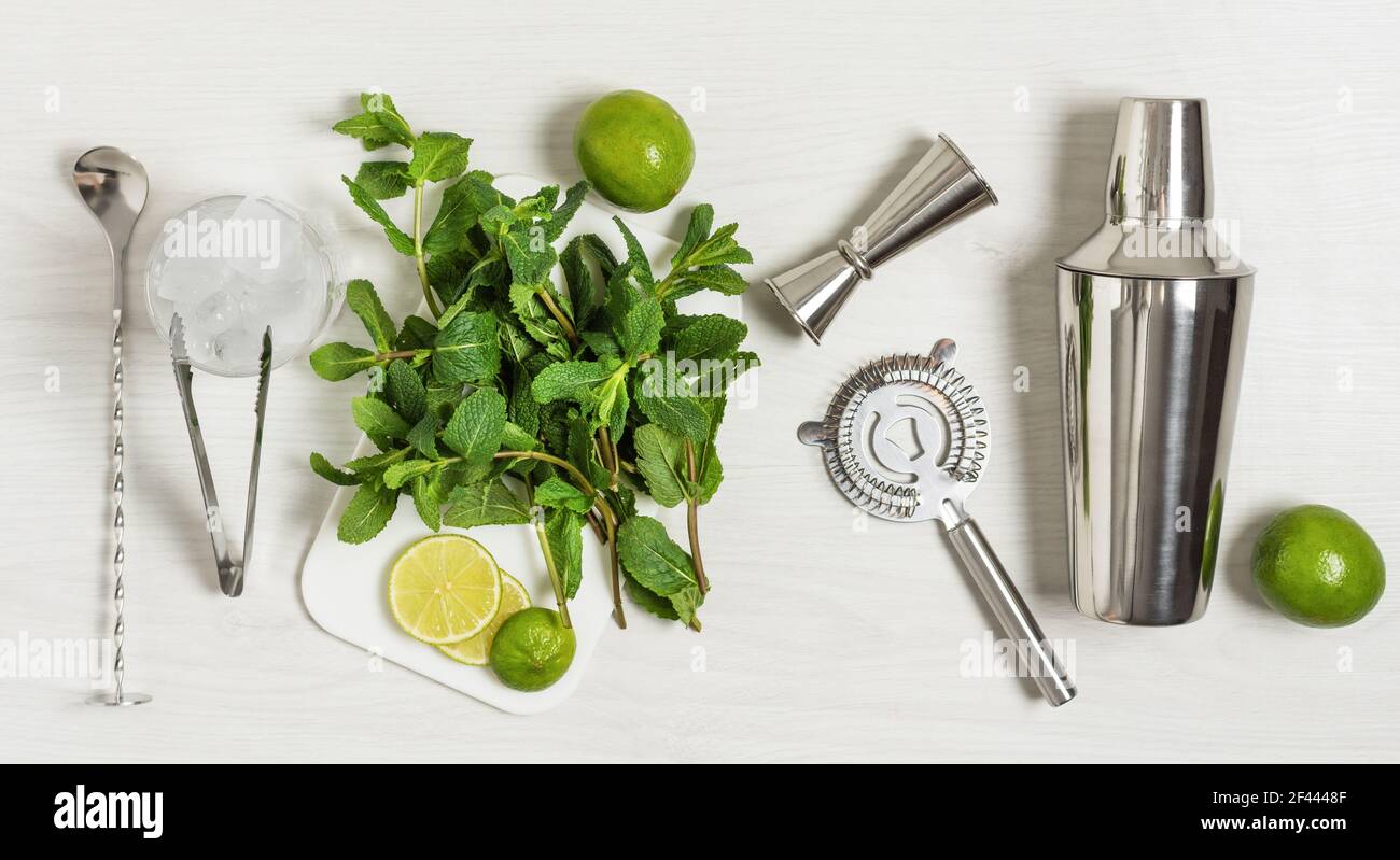 Ingrédients et ustensiles de bar pour préparer un cocktail de mojito avec  des glaçons, de la menthe fraîche et de la chaux sur fond de bois blanc.  Jeu d'accessoires de barre pour