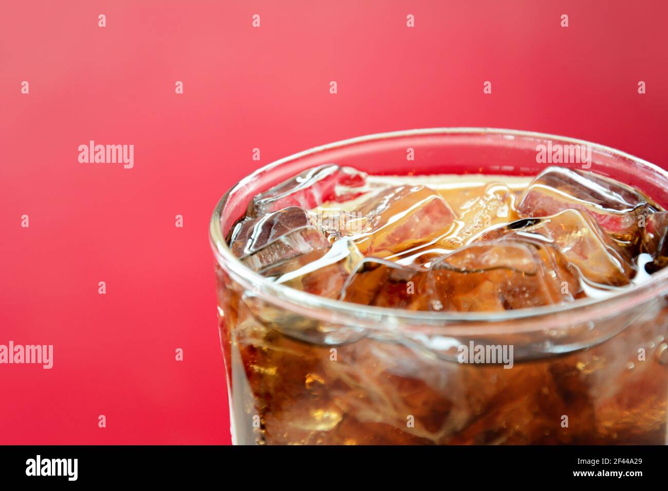 Un verre de boisson gazeuse au cola avec glaçons arrière-plan rouge Banque D'Images