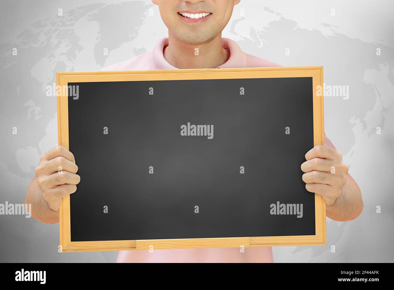 Tableau noir vierge tenu par un homme souriant sur fond gris Banque D'Images