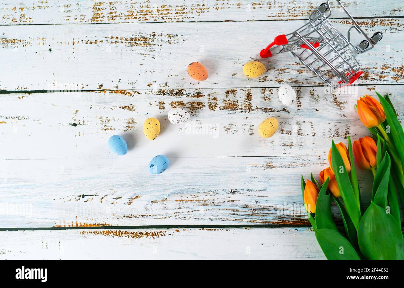 Les Pâques multicolores ont peint des œufs mouillés dans un panier sur une table en bois blanc avec des tulipes. Composition traditionnelle du printemps éléments de Pâques fleurs et oeufs pour le printemps. Décoration de printemps concept Banque D'Images