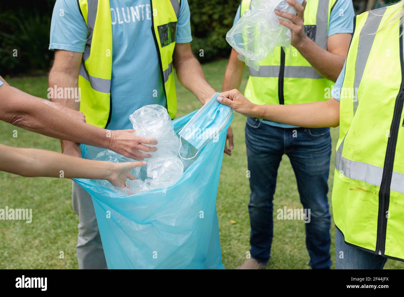 Section médiane du groupe multigénération caucasien collectant les déchets de plastique et masque facial dans le champ Banque D'Images