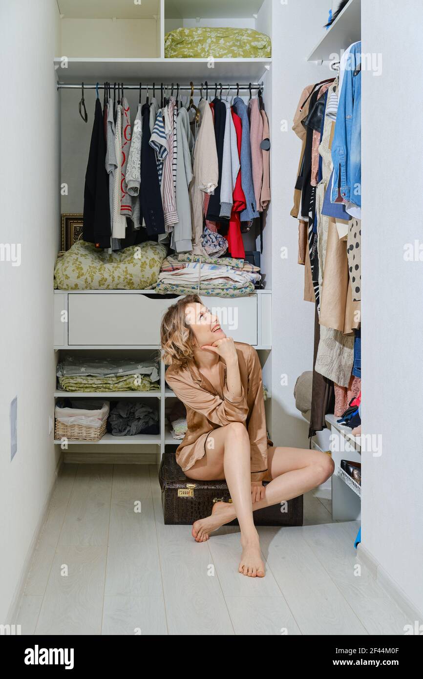 Une jeune femme heureuse est assise sur une vieille valise dans le dressing Banque D'Images