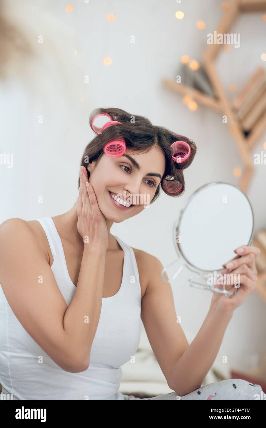Joyeuse femme en curlers regardant dans le miroir rond Banque D'Images