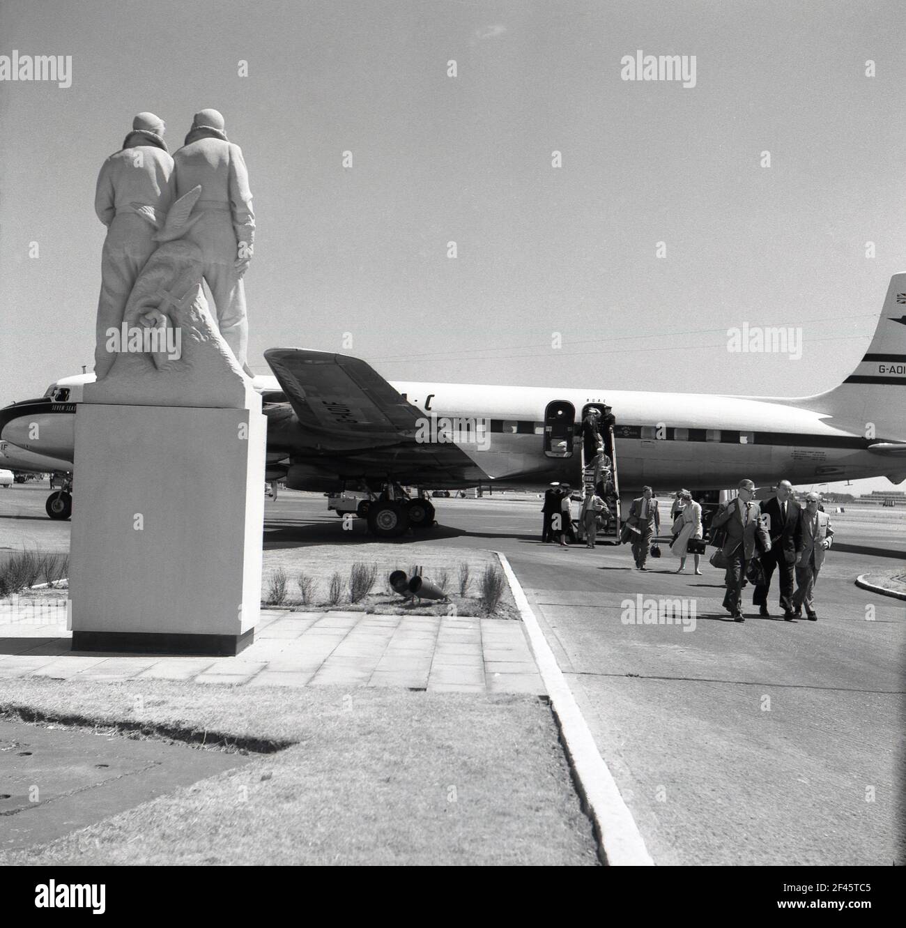 1960s, historique, aéroport de Londres et passagers au départ d'un avion à réaction BOAC passant devant un mémorial en pierre à WW2 pilotes RAF. Banque D'Images