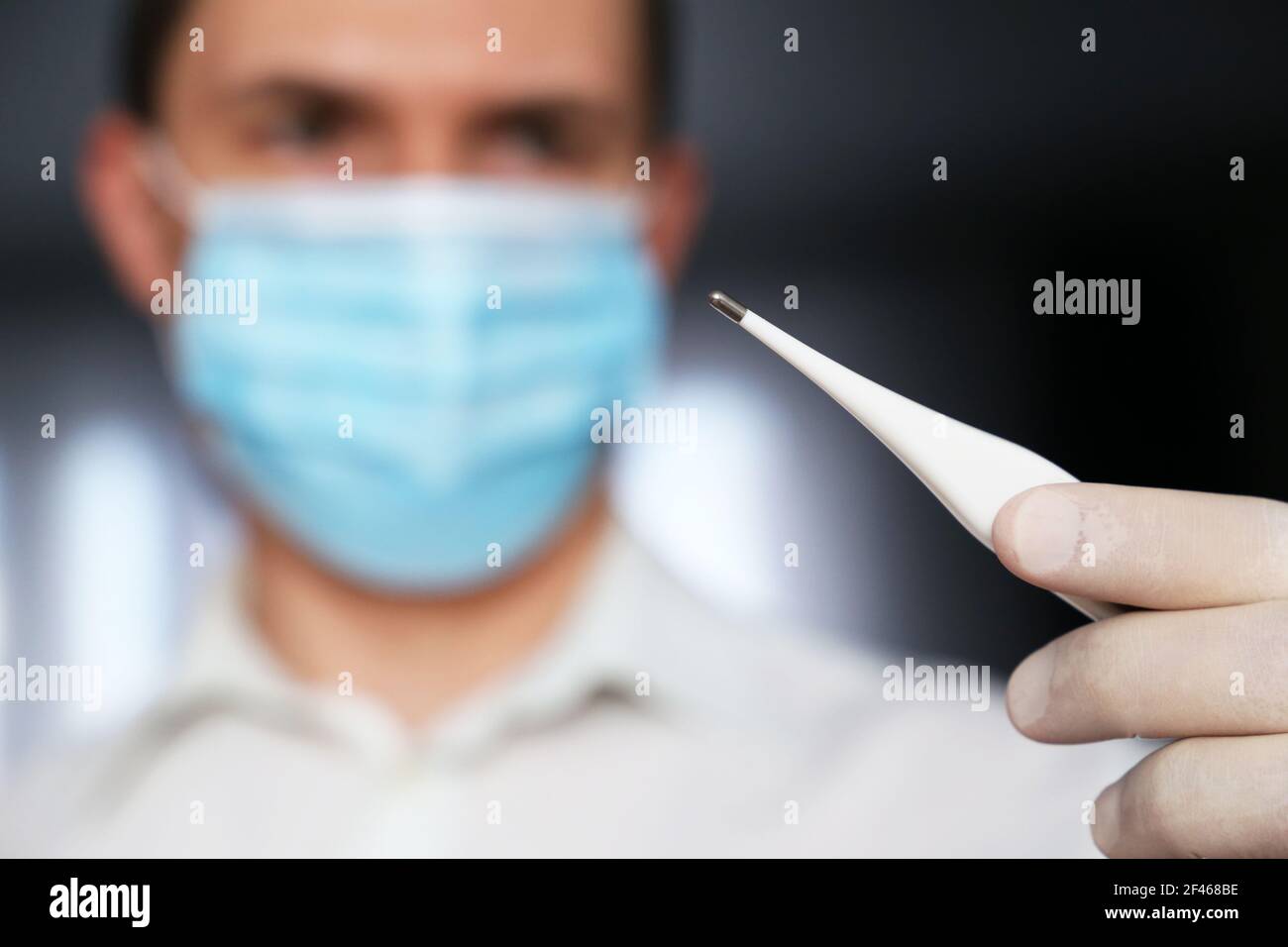 Symptômes du coronavirus, l'homme en masque médical mesure la température corporelle. Docteur avec thermomètre numérique dans sa main, concept de quarantaine Covid-19 Banque D'Images