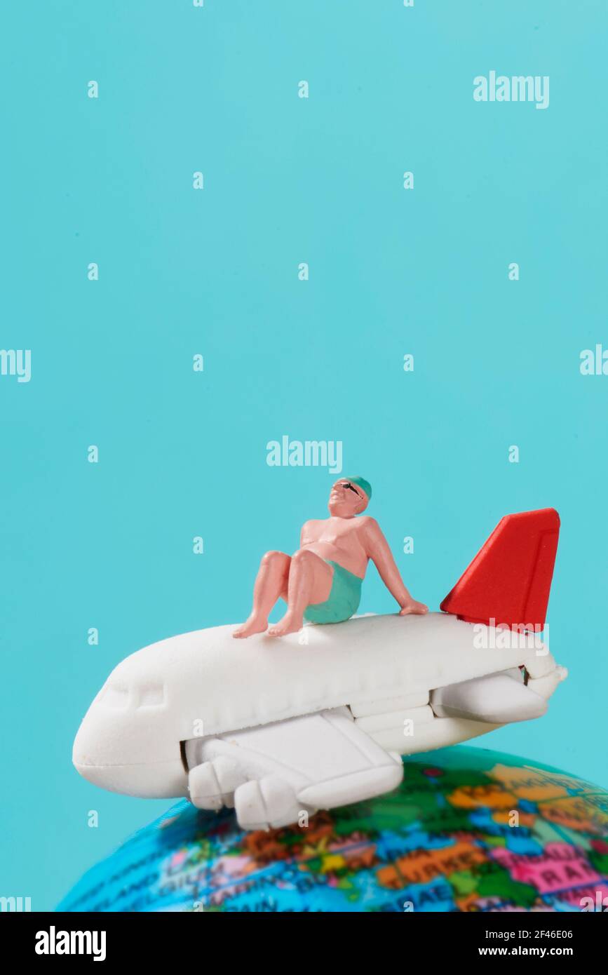 un homme miniature, portant un maillot de bain, est assis au-dessus d'un avion et d'un globe terrestre, sur un fond bleu simulant le ciel avec un peu de sp. vide Banque D'Images