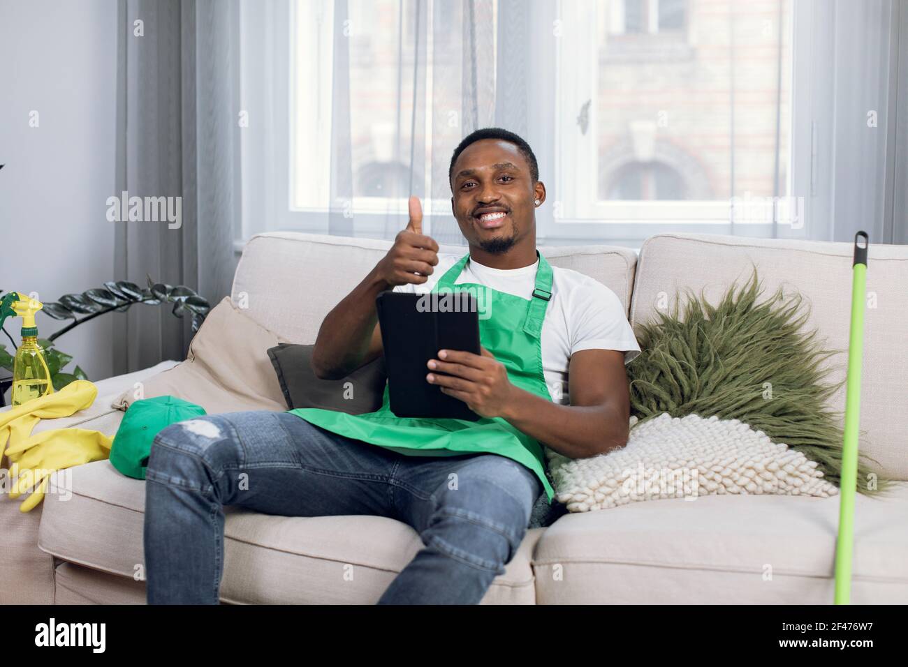 Concierge afro-américain souriant assis sur un canapé avec une tablette et montrant pouce vers le haut Banque D'Images
