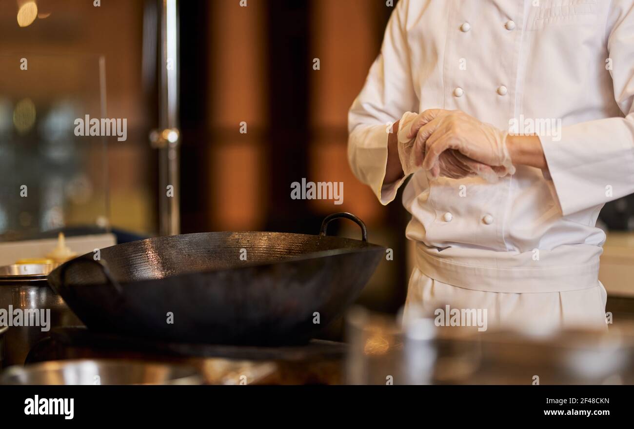 Chef en uniforme posant près du poêle avec wok dessus Banque D'Images