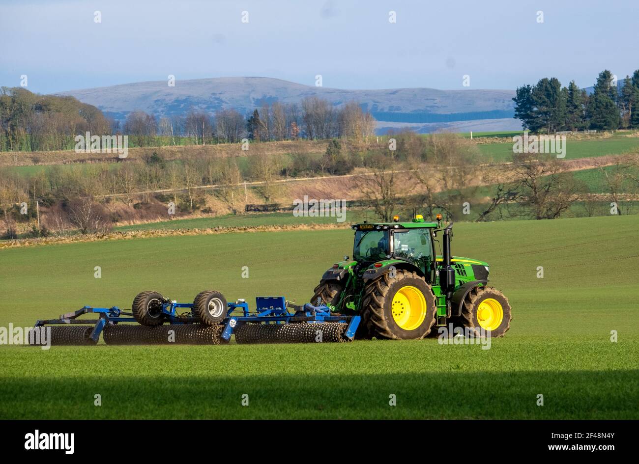 Un tracteur John Deere tire une machine de préparation de récolte sur un champ cultivé, West Lothian, Écosse. Banque D'Images