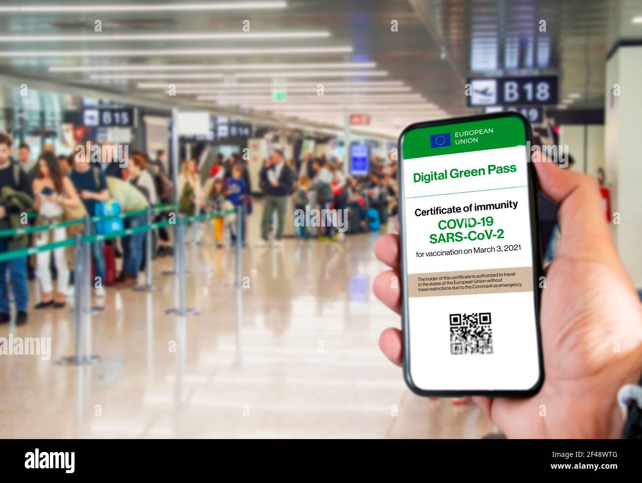 Le Digital Green Pass de l'Union européenne avec le code QR sur l'écran d'un mobile tenu par une main avec un aéroport flou en arrière-plan. ImmUnit Banque D'Images