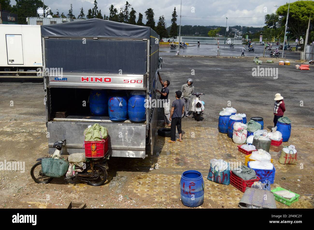 Da Lat (Dalat), province de Lam Dong, Vietnam - juillet 2015 : les hommes déchargent des barils en plastique bleu et des sacs avec de la glace du camion. Moto garée près d'un camion. Banque D'Images