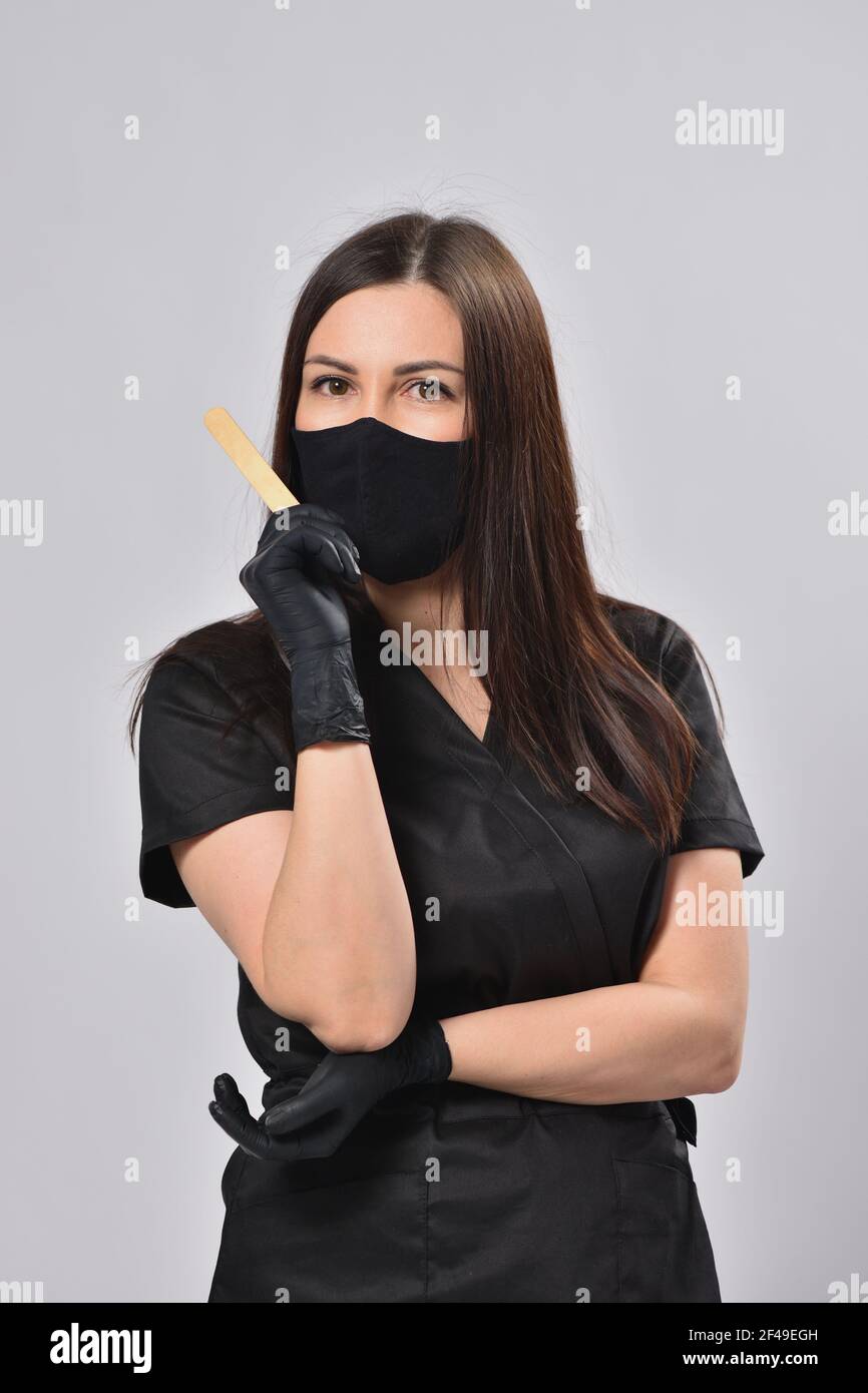 Femme esthéticienne en costume noir et masque facial tenant l'épilation bâton Banque D'Images