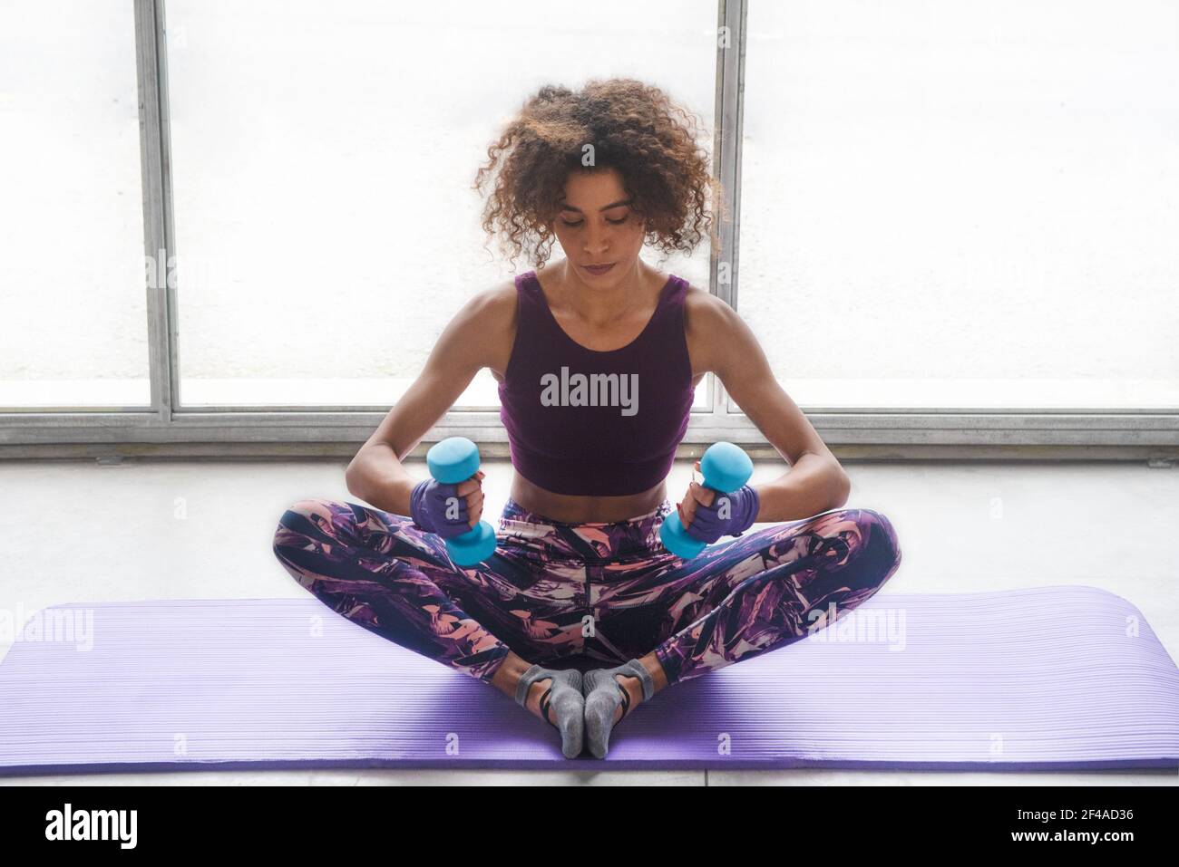Jeune belle femme faisant de l'exercice sur un tapis avec des haltères au sol d'une salle de gym intérieure. Arrière-plan horizontal blanc Banque D'Images