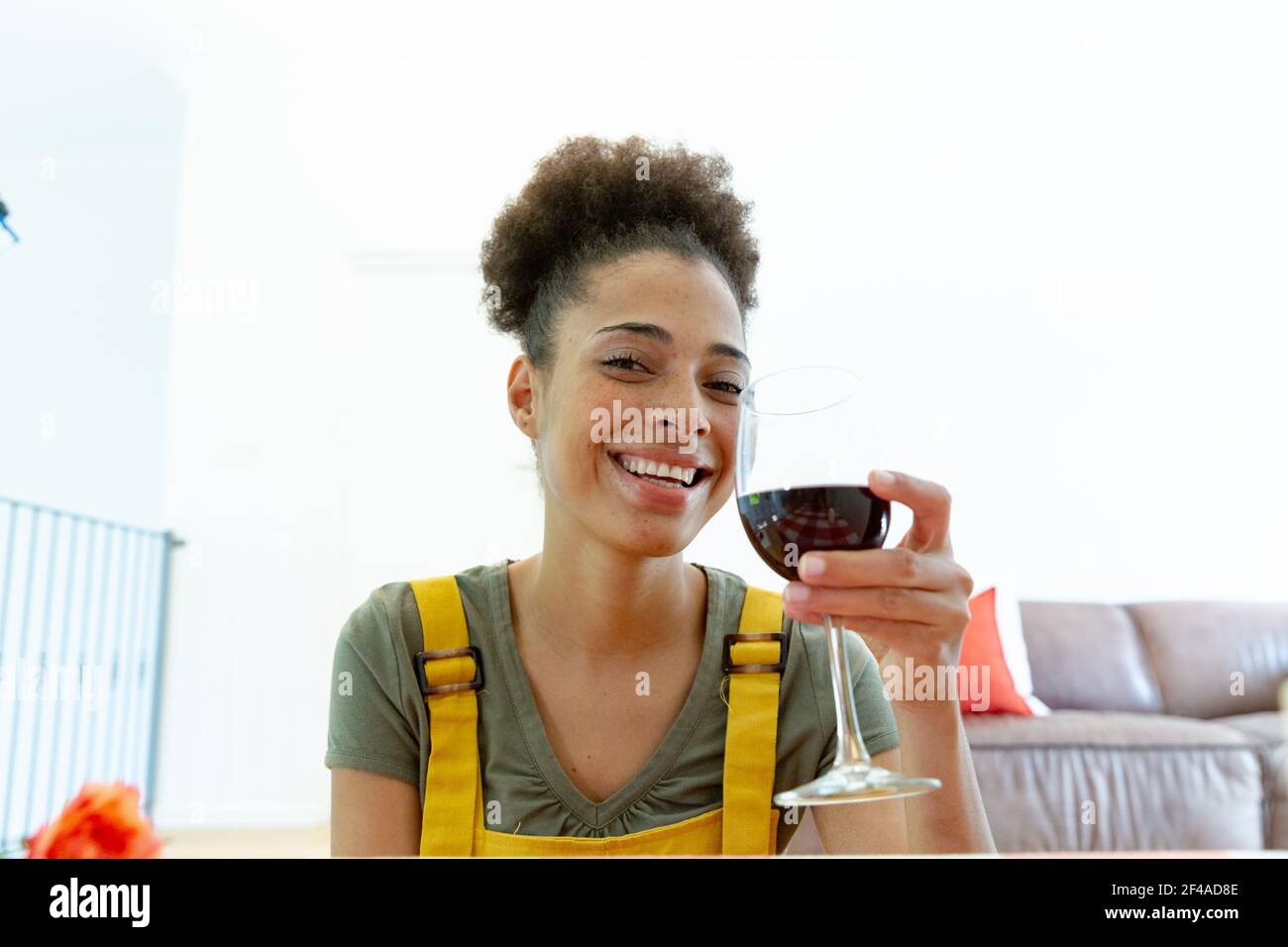 Femme de race mixte buvant un verre de vin et souriant à la maison Banque D'Images