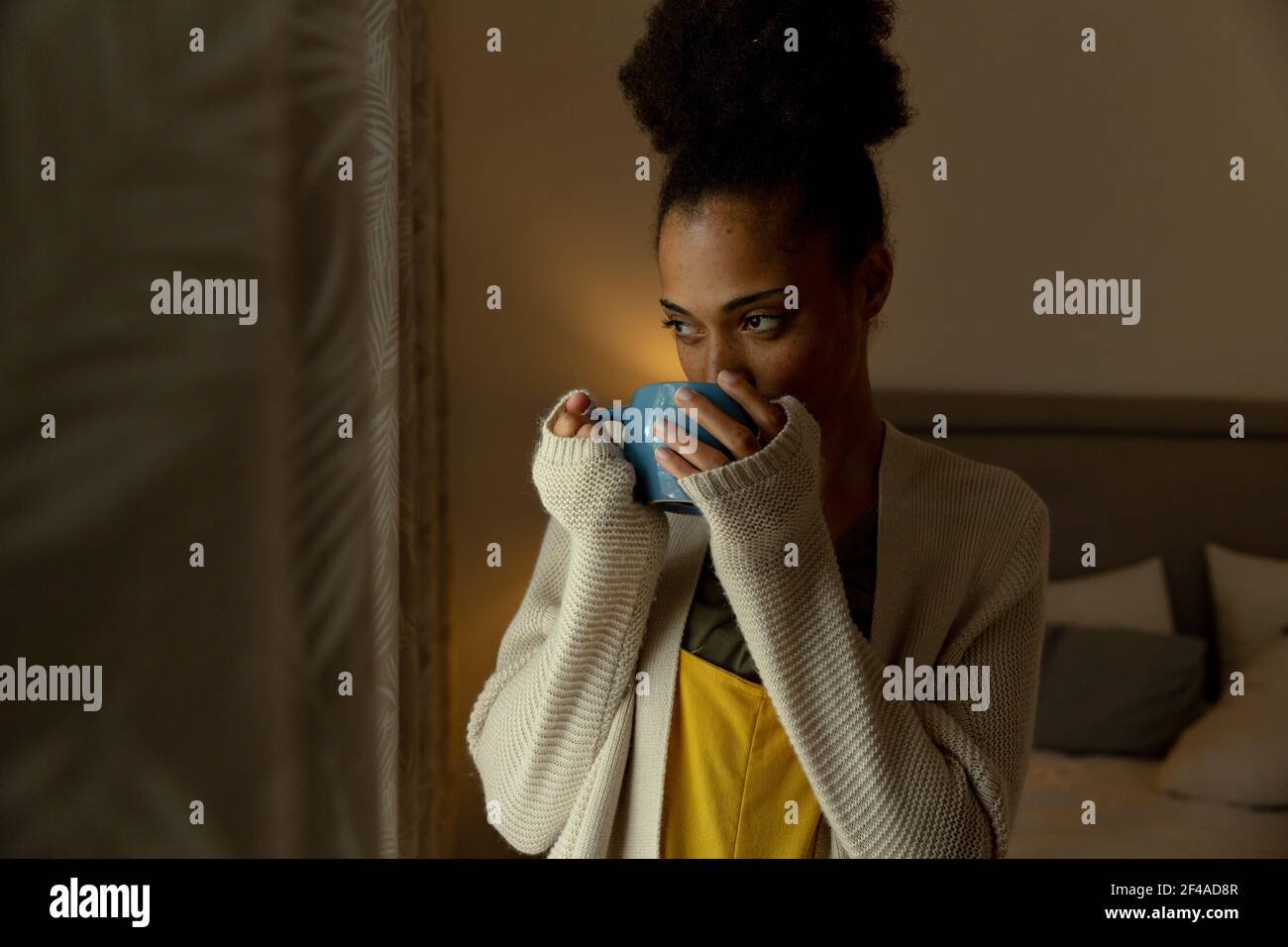 Femme de race mixte debout près d'une fenêtre et d'une tasse de boisson de café à la maison Banque D'Images