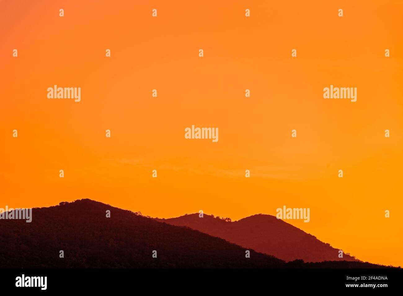 Montagnes à silhouette floue sous un ciel orange. Banque D'Images