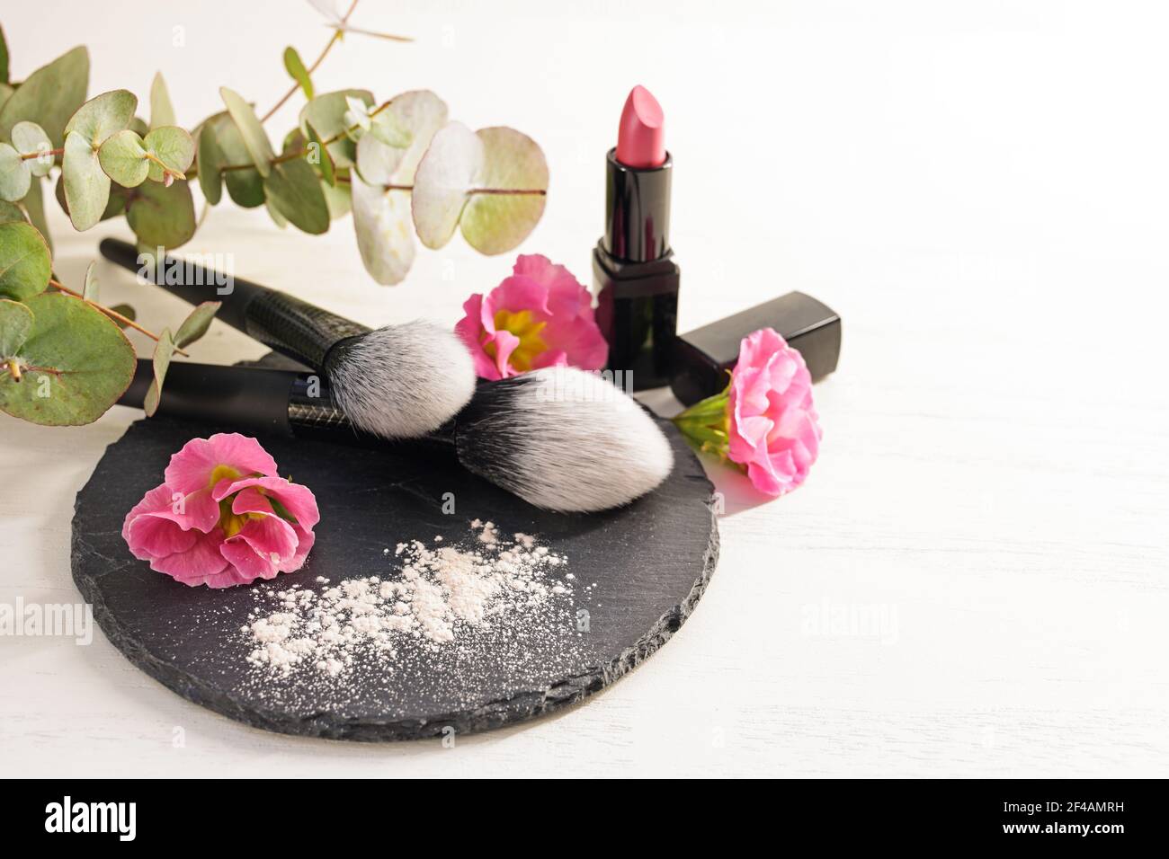 Pinceaux cosmétiques et poudre pour le visage sur une ardoise, rouge à lèvres rose et têtes de fleurs sur fond blanc, concept beauté et maquillage, espace de copie, sélection Banque D'Images