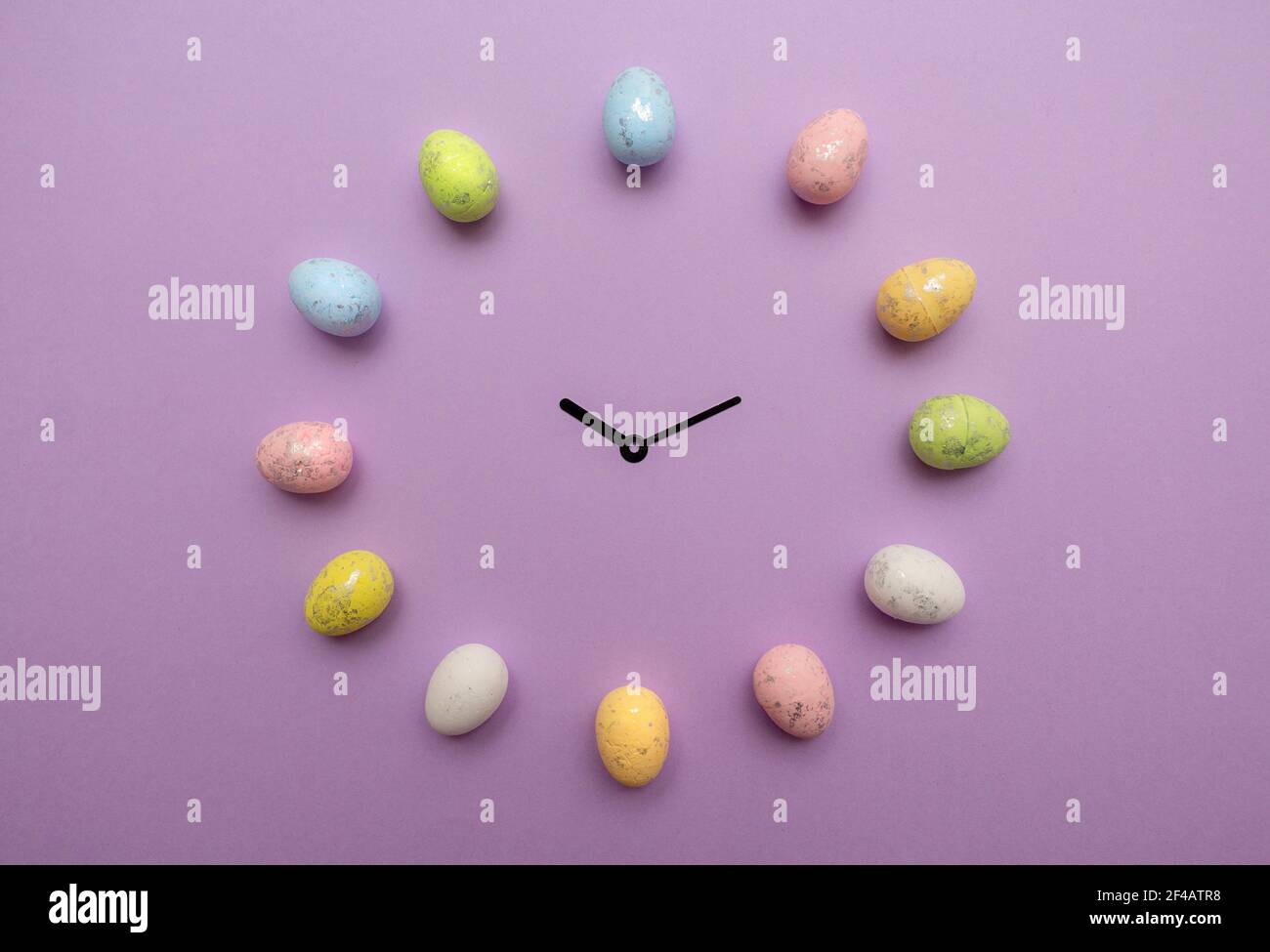 Les œufs de Pâques colorés forment une horloge avec les mains de l'horloge au milieu sur fond violet. Concept vacances de printemps Banque D'Images