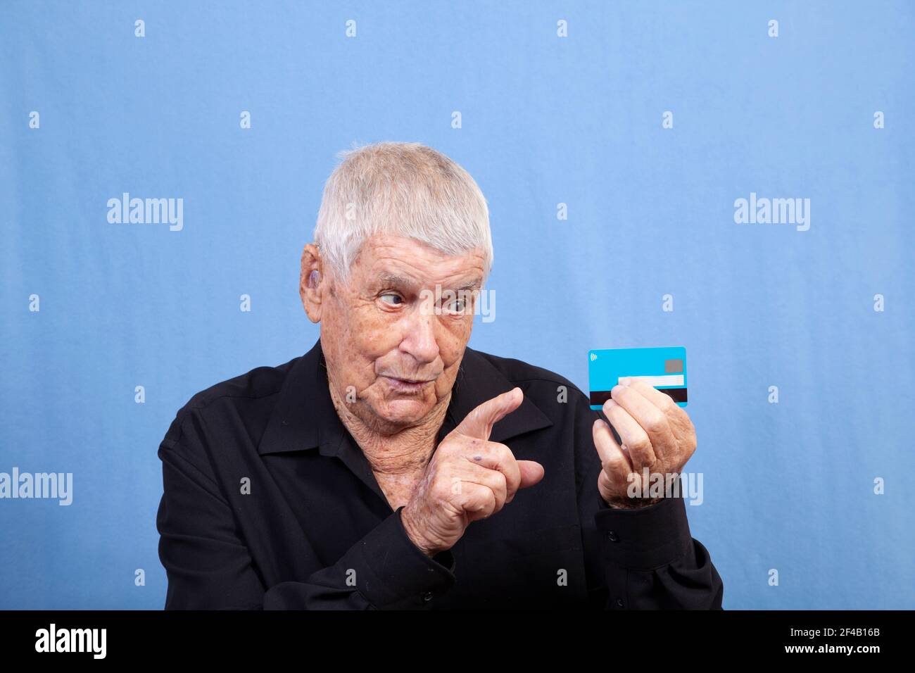 Un vieil homme âgé âgé âgé avec des cheveux gris, une peau endommagée par le soleil et une prothèse auditive regardant sa carte de crédit ou sa carte de crédit et pointant un doigt. Banque D'Images