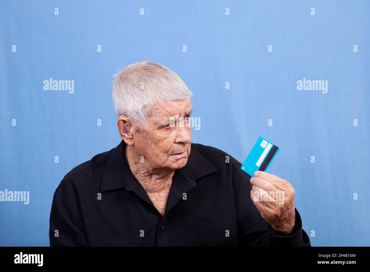 Un vieil homme âgé âgé âgé avec des cheveux gris, une peau endommagée par le soleil et une prothèse auditive qui semble perplexe à propos de sa carte de crédit ou de sa carte de crédit, peut-être en se demandant pourquoi elle ne va pas Banque D'Images