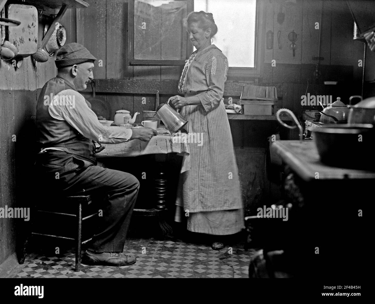 Femme qui verse une boisson pour un homme assis à une table dans une maison dans la Manche large, Queens CA. 1910-1915 Banque D'Images