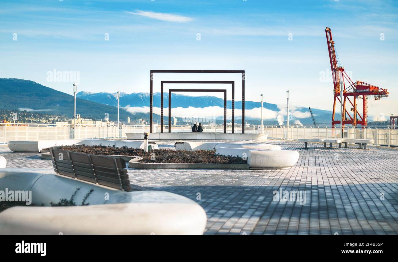 Deux personnes assises au bord de l'eau. Tôt le matin. Regardez Canada place, centre-ville de Vancouver, C.-B., Canada. Une grue de chargement est visible et visible Banque D'Images