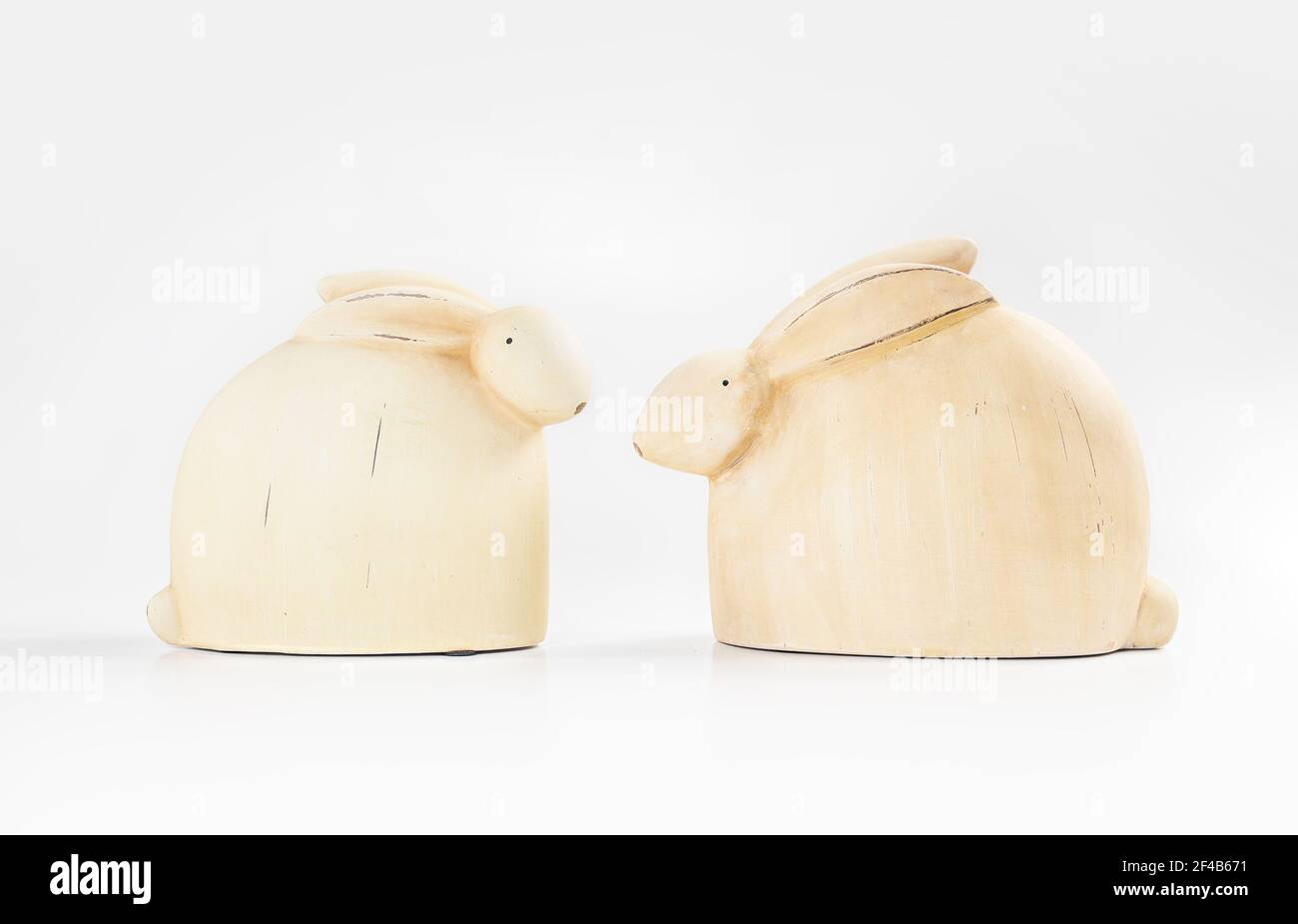 Vue sur les lapins en bois. Deux adorables petits lapins simples se faisant face l'un à l'autre. Couleur blanc ou jaune avec arrière-plan blanc pâle. Décoration de table sur le thème de Pâques Banque D'Images