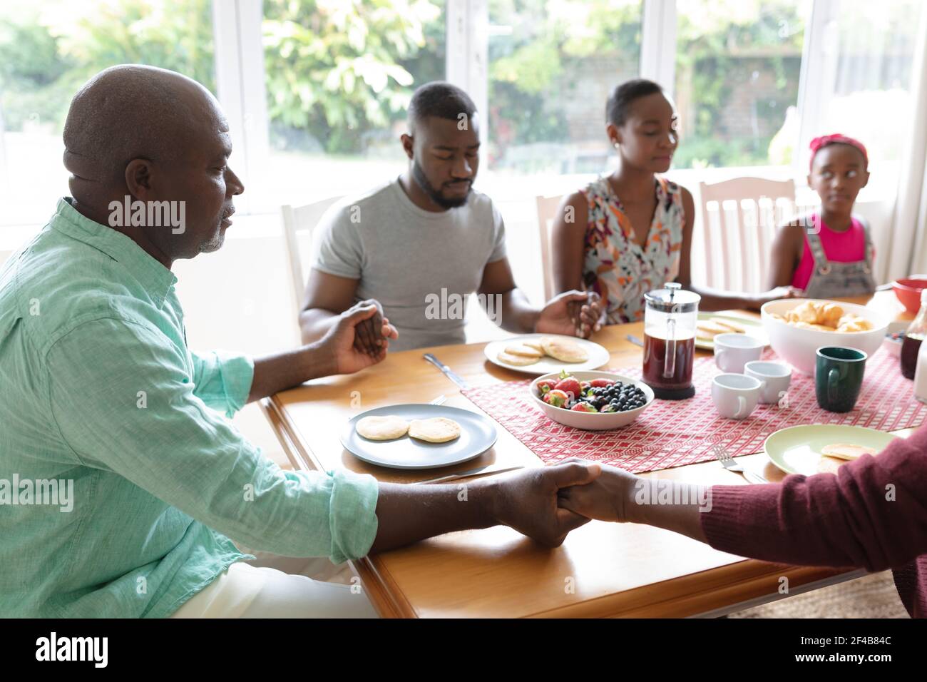 Parents, fille et grands-parents afro-américains assis tenant la main dans la prière à table du dîner Banque D'Images