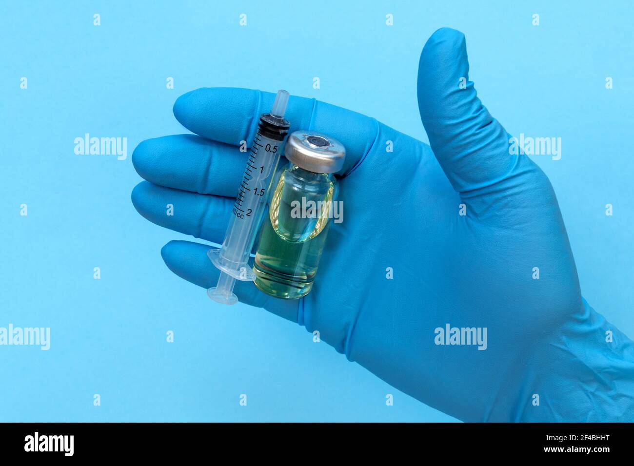 Main du médecin en gants bleus tenir le flacon avec un vaccin ou un médicament sur fond blanc. Concept d'étude de vaccination contre le coronavirus. Banque D'Images