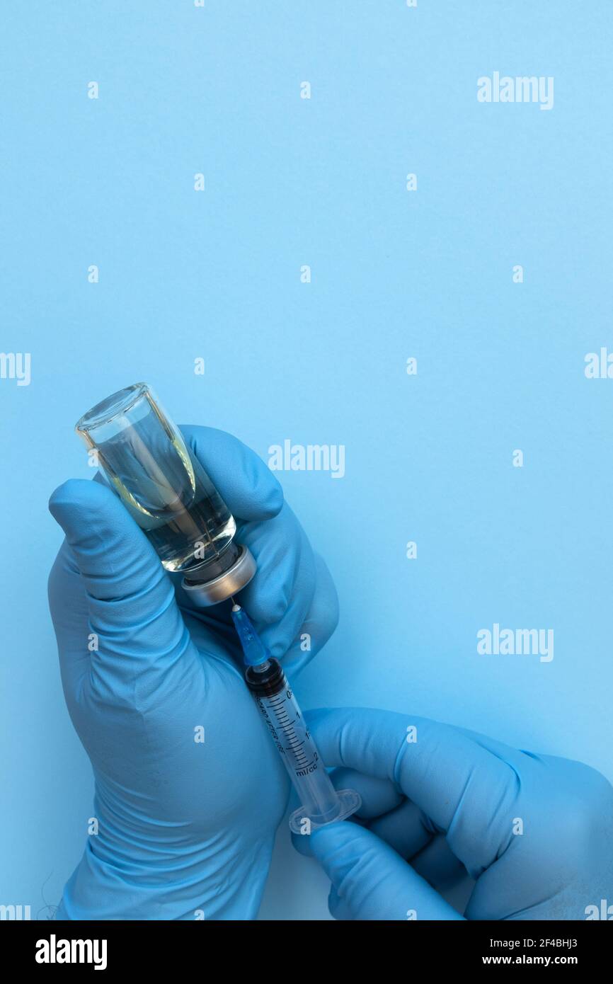 Main du médecin tenant le flacon de médicament et la seringue pour le vaccin au patient sur fond bleu. Vaccination contre le coronavirus traitement de la grippe la vaccination concep Banque D'Images