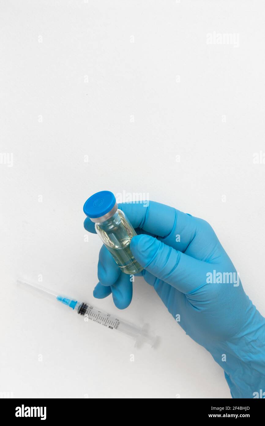 Main du médecin en gants bleus tenir le flacon avec un vaccin ou un médicament sur fond blanc. Concept d'étude de vaccination contre le coronavirus. Banque D'Images