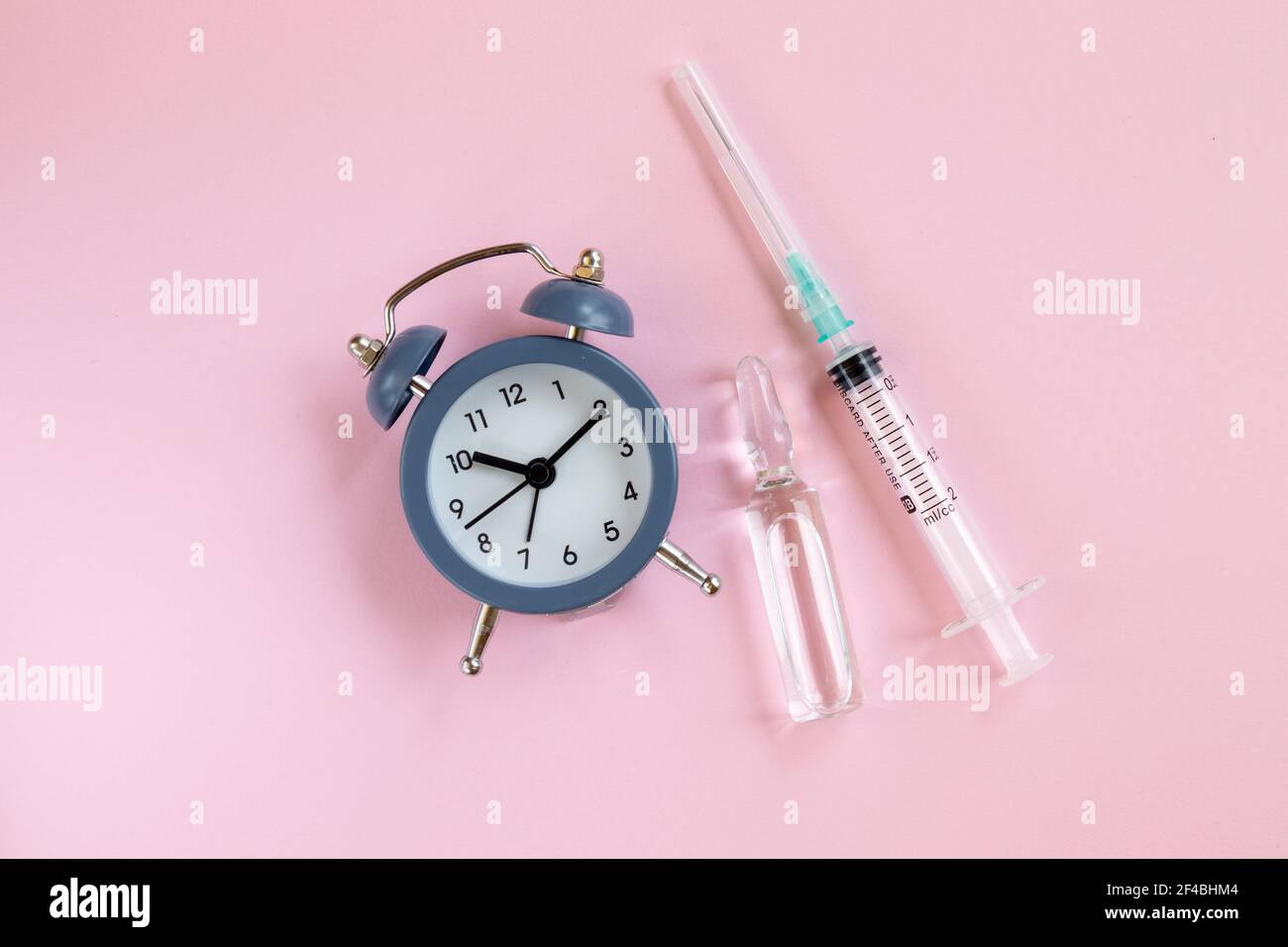 Il est temps de faire une injection. Réveil, seringue et ampoule sur fond rose. Vue de dessus. Plat Banque D'Images