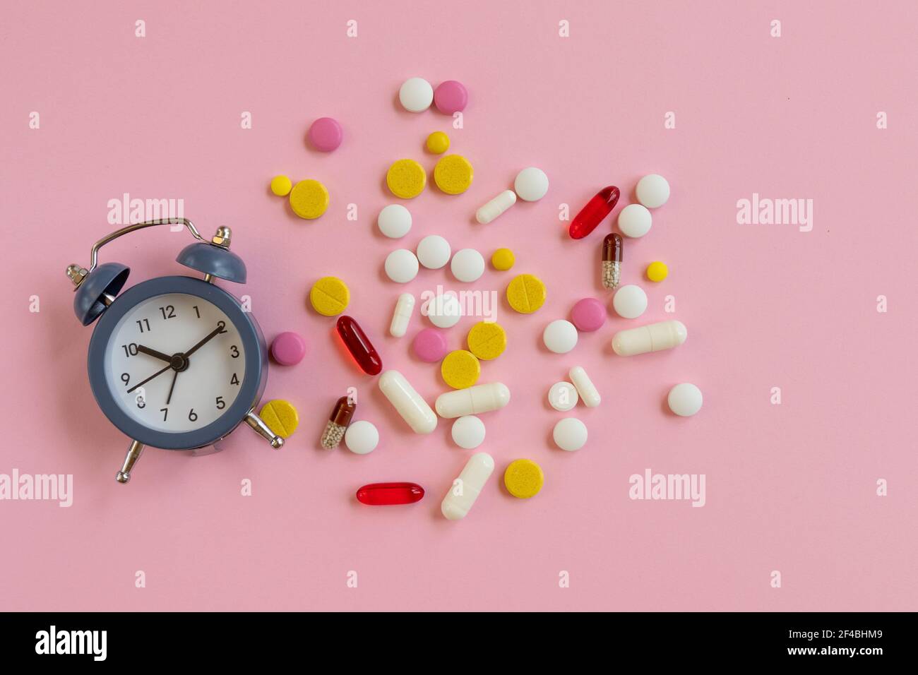 Beaucoup de pilules différentes avec réveil sur un fond rose. Il est temps de prendre le médicament. Vue du dessus Banque D'Images