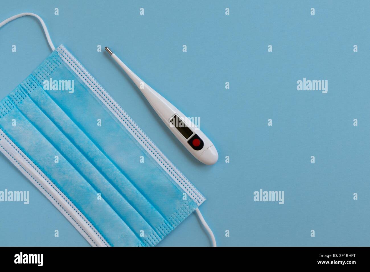 Masque chirurgical médical. Masque facial et thermomètre numérique sur fond bleu. Protection contre la grippe et le virus corona. Concept de soins de santé. Banque D'Images