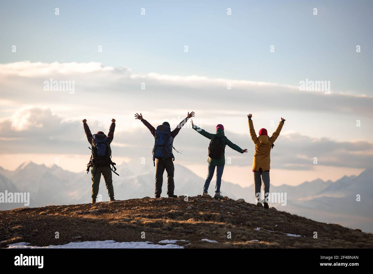 Quatre jeunes touristes sont debout avec des sacs à dos dans les poses de gagnant au sommet de la montagne Banque D'Images