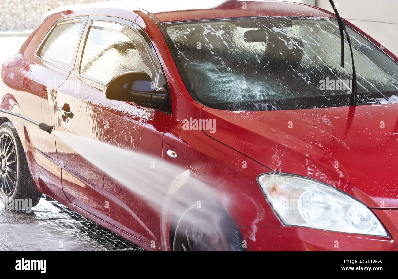 Voiture rouge lavée dans un lave-auto libre service, pulvérisation d'eau sur les côtés et la roue avant Banque D'Images